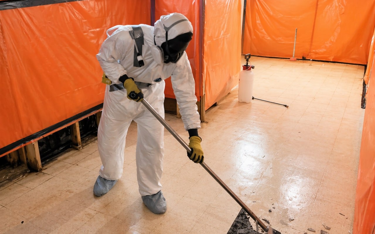 Technician in Tyvek suit and respirator performing asbestos cleanup